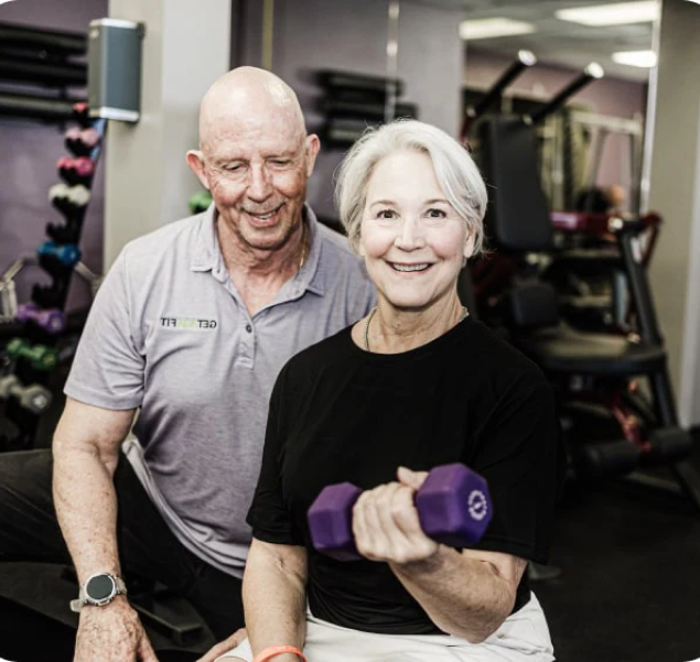Woman exercising with a dumbbell beside a trainer at Get Age Fit